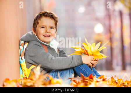 Felice ragazzo seduto nella pila di foglia con bouquet di autunno Foto Stock