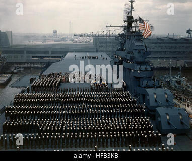 USS Yorktown (CV-10) Equipaggio sorge presso l'attenzione come il National Ensign è sollevato, durante la messa in servizio cerimonie presso la Norfolk Navy Yard, Virginia, 15 aprile 1943. Yorktown è dipinta di fresco in camuffamento di misura 21. Due acciaio-scafo sommergibile chasers (PC) sono a destra sull'altro lato del molo. Fotografato dal tenente Charles Kerlee, USNR. Ufficiale DEGLI STATI UNITI Fotografia della marina militare, ora nelle collezioni di archivi nazionali. La messa in esercizio della USS Yorktown (CV-10) il 15 aprile 1943 Foto Stock