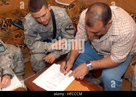 Stati Uniti Il personale dell'esercito Sgt. Samuel Lorenz con il 2° Brigata, 1a divisione di cavalleria, testimoni Salam trascorso Kadom firma per un micro concedere per il suo computer e il print shop, in Abu Ghraib, Iraq, maggio su 8. Un micro grant è denaro dato da parte del governo degli STATI UNITI Il governo iracheno a titolari di aziende a migliorare i loro negozi e l'economia locale. Micro concedere pay out di Abu Ghraib 170806 Foto Stock