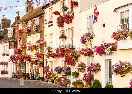 Inghilterra, trattativa. Vista lungo la riga del XVII e XVIII secolo edifici lungo il lungomare, tutti decorati con fiori di colore rosso nelle caselle. Il pittoresco. Soleggiato. Union Jack. Foto Stock