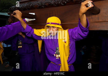 Antigua Guatemala - 16 Aprile 2014: il giovane uomo che indossa un porpora e giallo accappatoio, portante un galleggiante (EUN) durante le feste pasquali Foto Stock