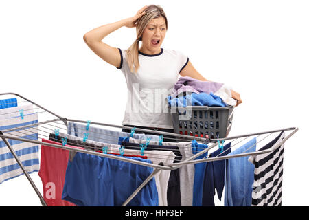 Donna con un cesto per la biancheria tiene il capo incredula e guardando a un rack di abbigliamento essiccatore isolato su sfondo bianco Foto Stock
