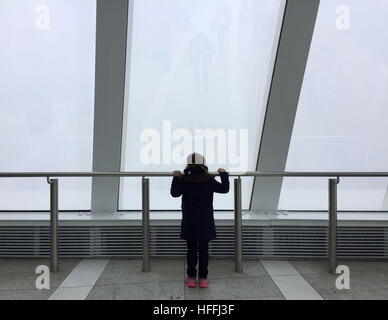 Una giovane ragazza guarda il coperto nebbia sullo skyline di Londra da Sky Garden in 20 Fenchurch Street a Londra, dopo forecasters avvertito di visibilità bassa come 100 metri con nebbia e temperature sotto zero attraverso filiere dell'Inghilterra. Foto Stock