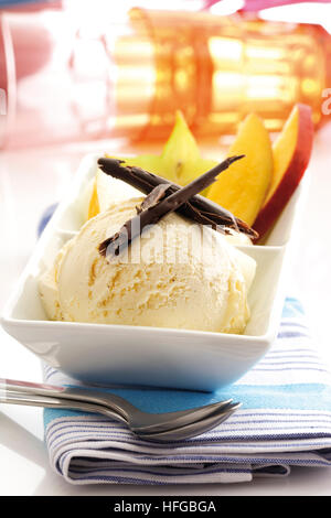 Coppa di gelato alla vaniglia guarnita con scaglie di cioccolato, fette di mango e starfruit Foto Stock