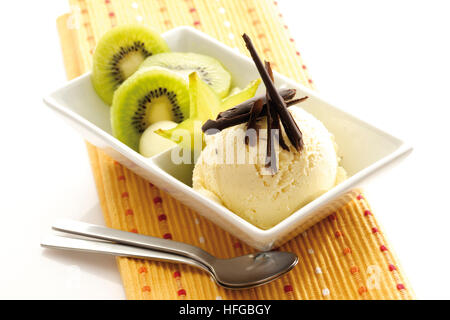 Coppa di gelato alla vaniglia guarnita con scaglie di cioccolato, fette di kiwi e starfruit Foto Stock