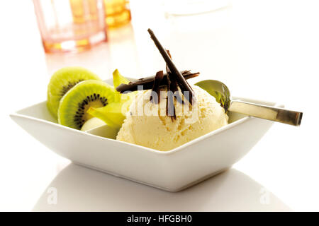 Coppa di gelato alla vaniglia guarnita con scaglie di cioccolato, fette di kiwi e starfruit Foto Stock