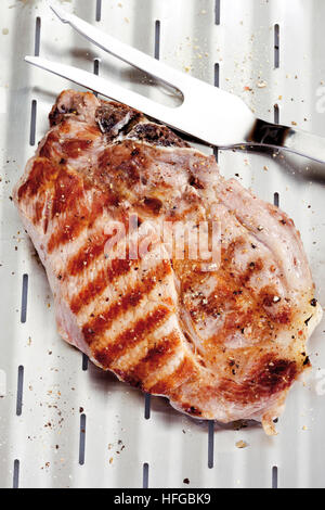 Carne di maiale alla griglia cotoletta, grill marchi, su una griglia in alluminio con forcella di carne Foto Stock