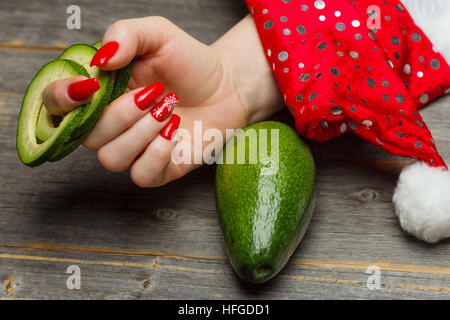 La mano femminile con belle festive Capodanno manicure trattiene il frutto di Avocado tagliato da anelli Foto Stock