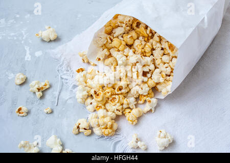 Dolce caramello popcorn in un sacchetto di carta sul cemento grigio. Foto Stock