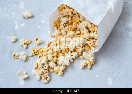 Dolce caramello popcorn in un sacchetto di carta sul cemento grigio. Foto Stock