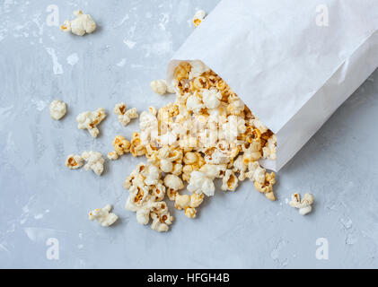 Dolce caramello popcorn in un sacchetto di carta sul cemento grigio. Foto Stock