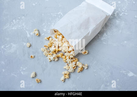 Dolce caramello popcorn in un sacchetto di carta sul cemento grigio. Foto Stock