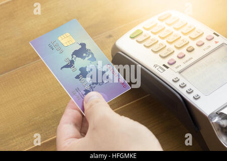 Mano del cassiere in possesso di una carta di credito e EDC macchina o terminale carte di credito. Carta di credito concetto e il terminale sul legno. Foto Stock