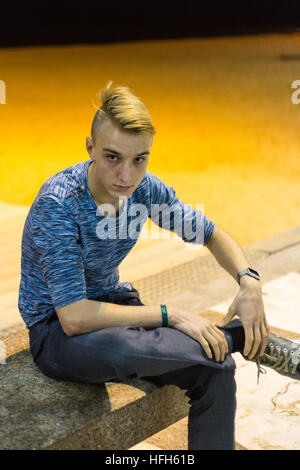Benidorm, Spagna. Il 31 dicembre, 2016. I turisti e i locali, goditi la musica e le danze sul lungomare e la spiaggia. giovane uomo si siede sul banco di pietra, capelli biondi breve ritagliato con maglia blu, maglione, ponticello. Foto Stock