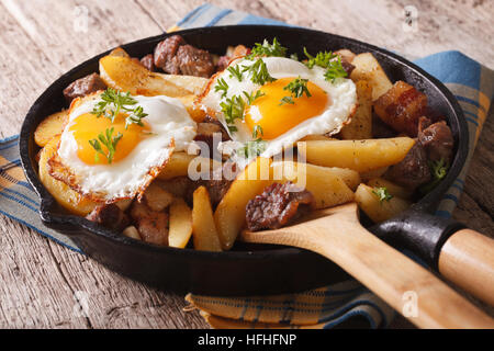 Cucina europea: patate fritte con carne, uova e bacon in una padella di close-up orizzontale. Foto Stock