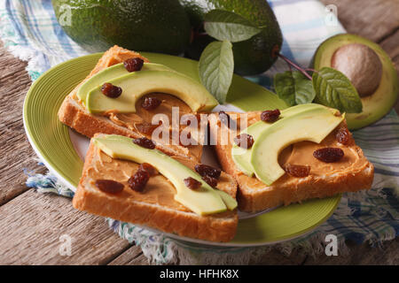 Un sano panino con burro di arachidi, avocadi e uvetta close-up su una piastra orizzontale. Foto Stock