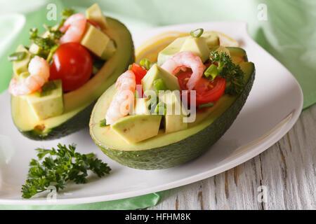 Avocado farcito con gamberi e pomodori close-up su una piastra orizzontale. Foto Stock