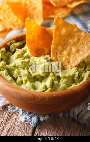 Guacamole e nachos chips macro in una ciotola di legno. Verticale, stile rustico Foto Stock