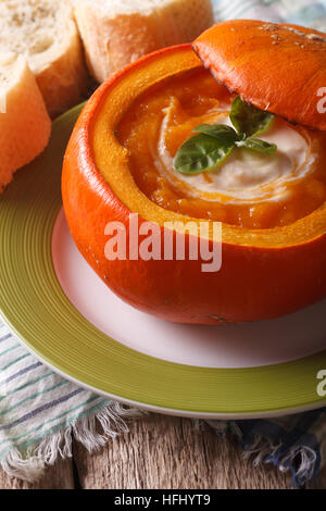 Zuppa di purea in una zucca al forno con panna acida e basilico close-up. In verticale Foto Stock