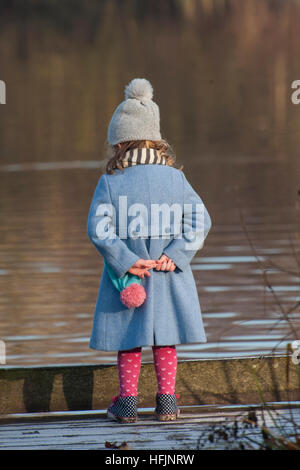 Una bambina molto intelligente vestiti ispeziona l'acqua in un lago Foto Stock