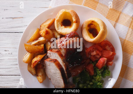 Domenica: arrosto di maiale con patate, verdure e Yorkshire pudding sulla piastra closeup. vista orizzontale dal di sopra Foto Stock