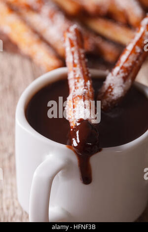 Lo spagnolo churros immerso in una tazza di cioccolata calda una macro sul piano verticale. Foto Stock