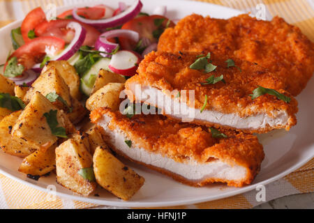 Tagliate a fette cotoletta di maiale, insalata e patate fritte su una piastra di close-up orizzontale. Foto Stock