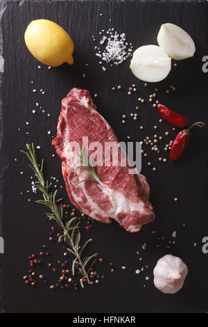 Un pezzo di carne di maiale cruda collo, spezie e verdure close-up su una scheda di ardesia. verticale vista superiore Foto Stock