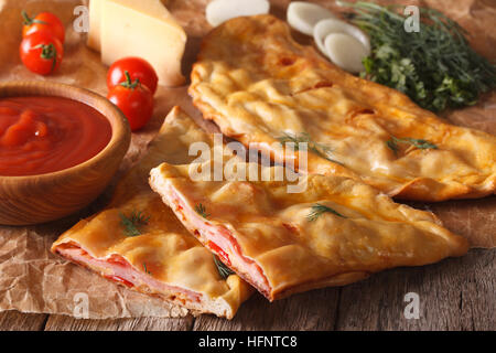 Tagliare la pizza italiana calzone con prosciutto e formaggio vicino sul tavolo e ingredienti orizzontale. Foto Stock