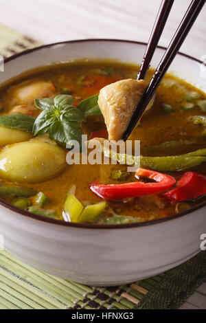 Curry verde tailandese con il pollo in una ciotola bianco macro verticale. Foto Stock