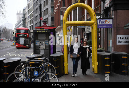 La gente a piedi attraverso la protezione temporanea barriere poste su Victoria Street nel centro di Londra, in vista del nuovo anno di celebrazioni, come migliaia di poliziotti fornirà un anello di protezione intorno alla città di pezzo i fuochi d'artificio, mentre le tattiche non sono stati adattati a seguito di tale anno le atrocità terroristiche in Europa. Foto Stock