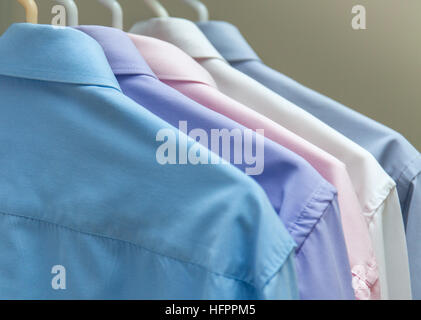 Luminose le camicie da uomo appeso su appendiabiti sfondo grigio Foto Stock
