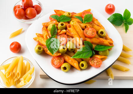 Piastra bianca di penne pasta decorate con pomodorini e olive ed erbe su un vassoio in legno Foto Stock