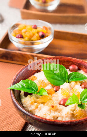 Vista ravvicinata di una vecchia ciotola di legno di sano di farina di avena con frutti di bosco, uvetta e erbe su una tovaglia di colore grigio con uno sfondo sfocato Foto Stock