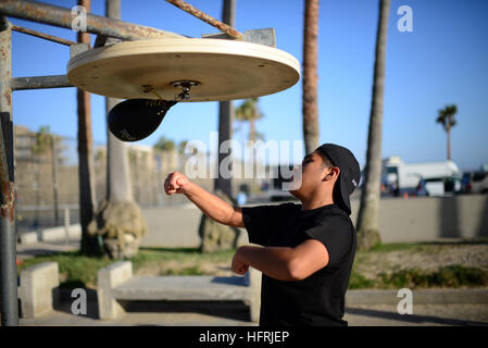 Giovane uomo a fare pratica con la boxe Speed bag sulla spiaggia di Venice, California. Foto Stock