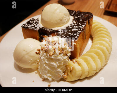 Decorate il miele e il cioccolato la lava su pane tostato con gelato alla vaniglia e di banana e panna montata nel ristorante della Thailandia Foto Stock