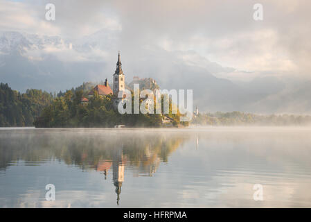 Chiesa sulla piccola isola del lago di Bled all alba di una mattinata nebbiosa in autunno con riflesso nell'acqua in Slovenia. Foto Stock