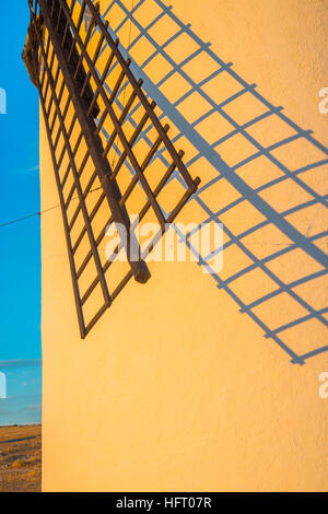 Mulino a vento, il braccio e la sua ombra sul muro dipinto di bianco al tramonto. Campo de Criptana, Ciudad Real Provincia, Castilla La Mancha, in Spagna. Foto Stock