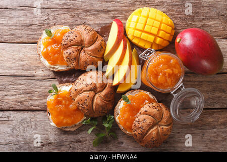 Dolci appena sfornati con mango marmellata, burro e menta vicino sul tavolo. Vista orizzontale dal di sopra Foto Stock