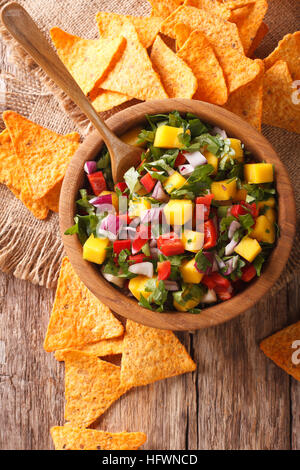 Salsa messicana con manghi, peperoni, il coriandolo e la cipolla vicino fino in una ciotola e corn chips sul tavolo. vista verticale da sopra Foto Stock