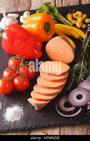 Materie patate dolci, peperoni, pomodori, cipolle, aglio, rosmarino e spezie vicino sul tavolo. In verticale Foto Stock