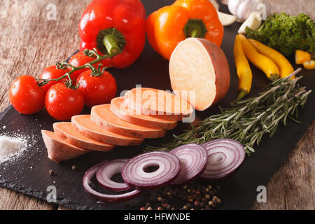 Materie patate dolci, peperoni, pomodori, cipolle, aglio, rosmarino e spezie vicino sul tavolo orizzontale. Foto Stock