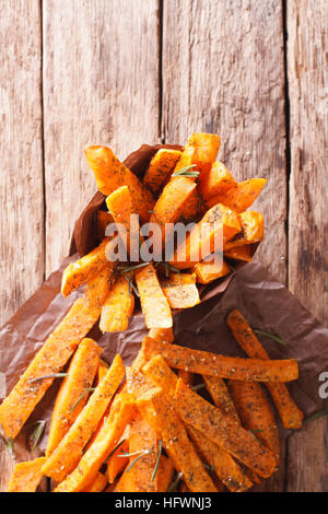 Arrosto di patate dolci con le erbe in un cono di carta vicino sul tavolo. vista verticale da sopra Foto Stock