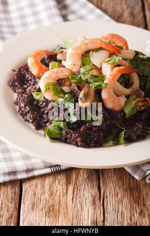 Il riso nero con gamberi, calamari, cozze e capesante sulla piastra closeup verticale.