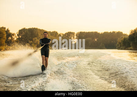 Uomo che cavalca wakeboard sull onda di motoscafo. Maschio di sci d'acqua dietro una barca sul lago. Foto Stock