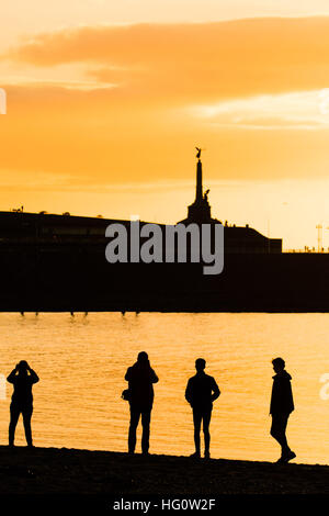 Aberystwyth, Wales, Regno Unito. Il 2 gennaio, 2016. Aberystwyth Wales UK, lunedì 02 gennaio 2017 UK Meteo: alla fine di un estremamente freddo, chiaro e gelido giorno, un gruppo di quattro persone stand in silhouette sulla spiaggia a Aberystwyth sulla West Wales coast di Cardigan Bay, Regno Unito, con il contorno della città distintivo del memoriale di guerra all'orizzonte foto © Keith Morris/Alamy Live News Foto Stock