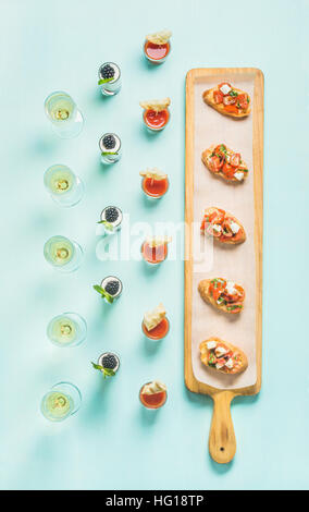 Spuntini, brushettas, gazpacho scatti, dessert, champagne pastello su sfondo blu Foto Stock