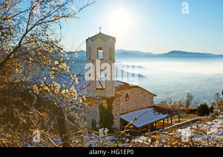 La vecchia chiesa ortodossa con un cimitero, circondato da un giardino d'inverno, con la valle di nebbia di Kastoria sullo sfondo, Grecia. Foto Stock