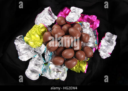 Pila di uova di pasqua di cioccolato scorporato dal colorato involucri di foglia contro uno sfondo nero. Foto Stock