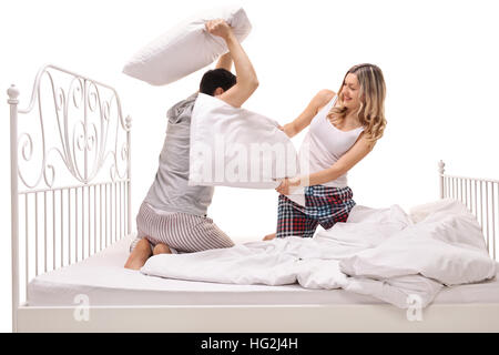 Giovane uomo e donna con un cuscino lotta su un letto isolato su sfondo bianco Foto Stock